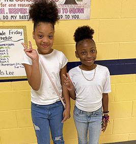 Two happy girls on twin day in the school hallway