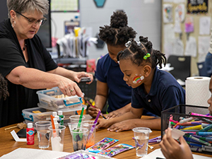 Adult helping two girls with their art project in the classroom